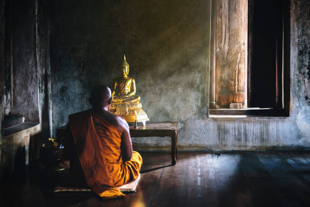 A monk is worshiping and meditating in front of the golden buddha as part of buddhist activitiesfocus on the buddha stock photo