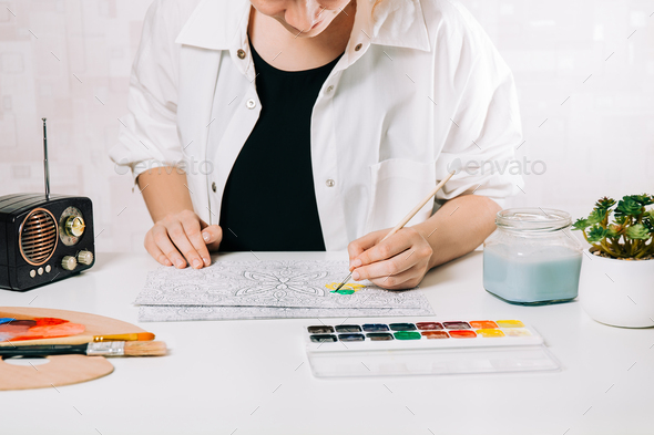 Woman paints a sketch by paintbrush meditative process of coloring pages self expression by art stock photo by jannissimo