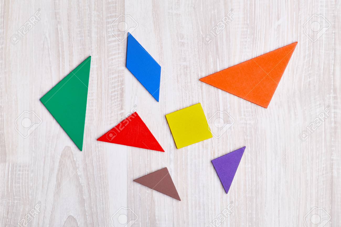 Colored geometric pieces of puzzle like triangles square and parallelogram are scattered on a light wooden background stock photo picture and royalty free image image