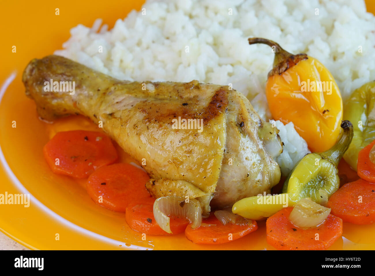 Pierna de pollo frito con arroz zanahorias y pimientos en la placa naranja fotografãa de stock