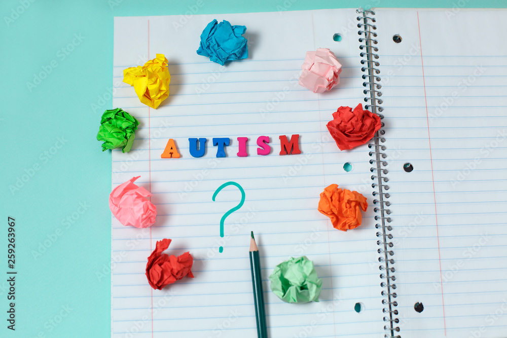 Autism colorful word from color wooden letters on notebook page and question mark with a pencil surrounded by crumpled colored papers concept image photo